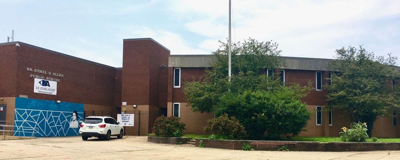 Front exterior of Dr. Ethel Allen School in Philadelphia, showing the two-story brick school building, main entrance, school sign, mural, and landscaped front courtyard.
